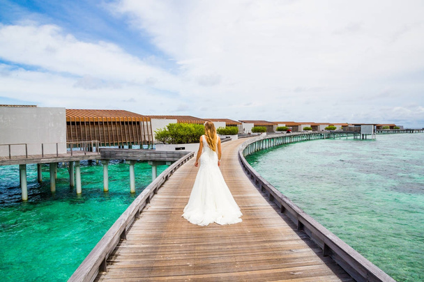 Beautiful bride in a long sexy white dress standing on a pier in the Maldives - Valokuva, kuva
