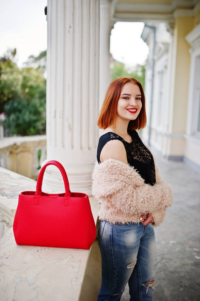 Red haired girl with red handbag posed near vintage house. - Φωτογραφία, εικόνα