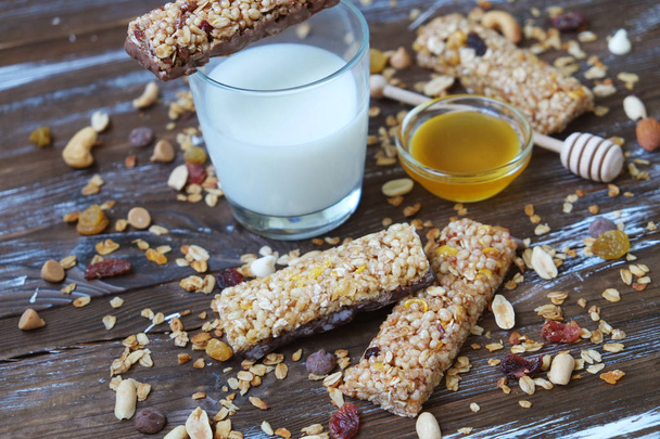 Cereal bars with dry fruits, nuts, granola and glass of milk on wooden background.Top view.Healthy homemade cereal bars with nuts, seeds and dried fruits on the wooden table. - Zdjęcie, obraz