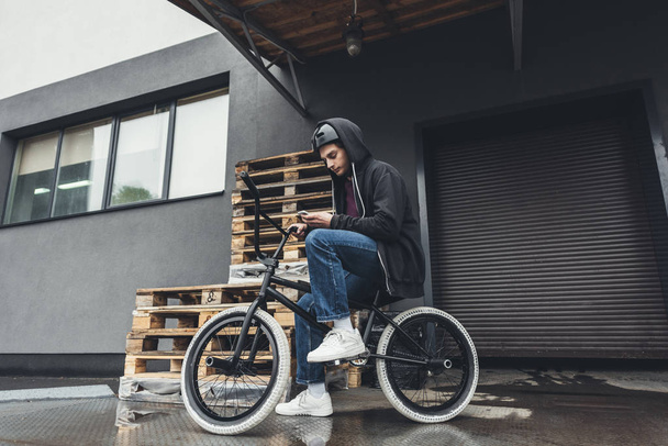 BMX ποδηλάτης χρησιμοποιώντας smartphone    - Φωτογραφία, εικόνα
