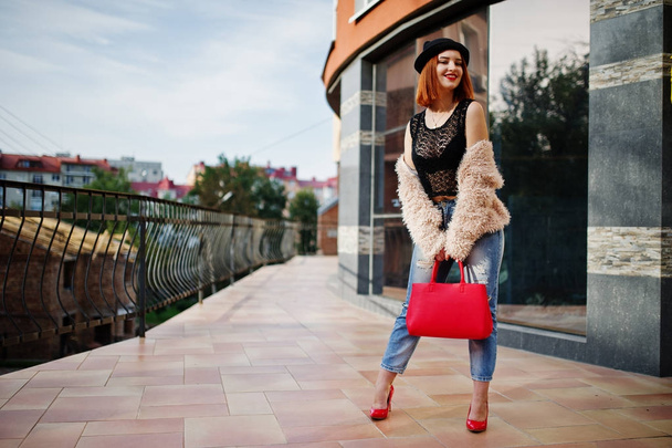 Red haired girl in  hat with red handbag posed near modern house - Фото, изображение