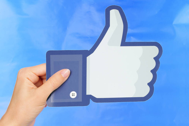Hand holds Facebook logo on blue paper background - Fotografie, Obrázek