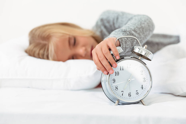Close-up of sleepy little girl turned off alarm clock in her bed - Valokuva, kuva