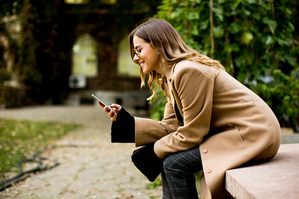 Młoda kobieta siedzi odkryty i przy użyciu telefonu komórkowego - Zdjęcie, obraz