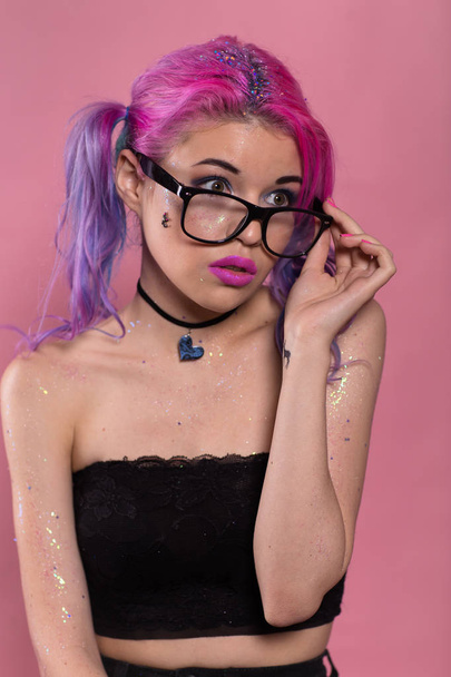 Portrait of young attractive woman with heavy makeup in black top and heart-shaped choker. Holding her black eyeglasses in hand and looking away. - Zdjęcie, obraz