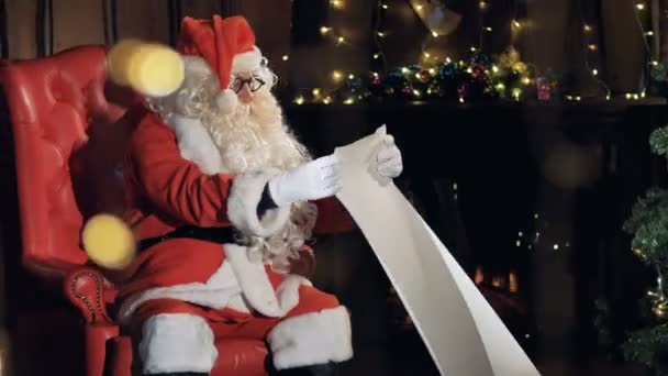 Santa in his chair near Christmas tree reading new year gift list. - Metraje, vídeo