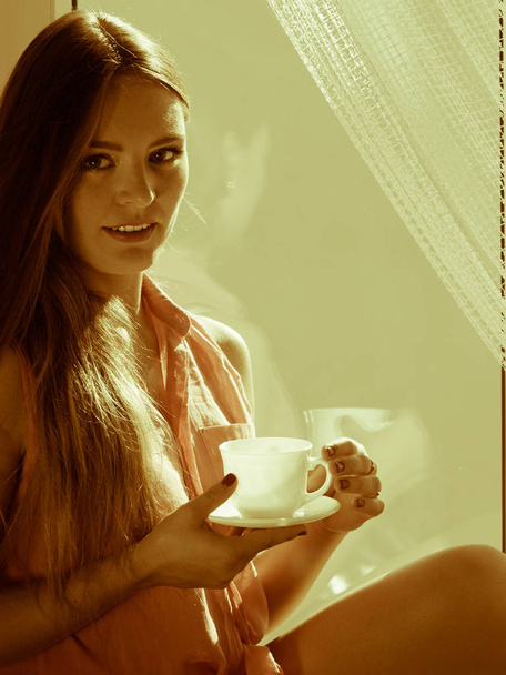 Mulher olhando através da janela, relaxante beber café
 - Foto, Imagem