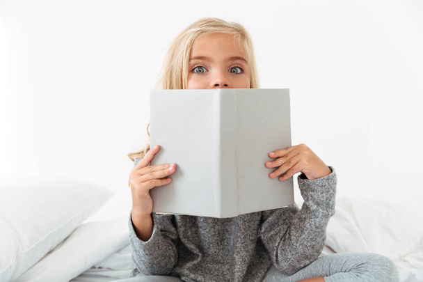 Close-up portrait of charming girl covering her face with book,  - Fotografie, Obrázek