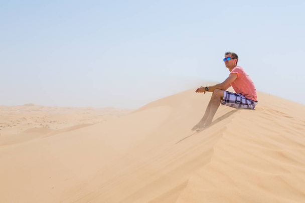 Young boy sitting in a desert with sunglasses - Zdjęcie, obraz