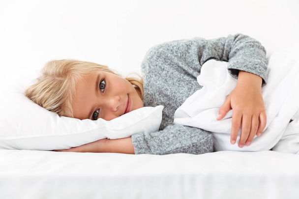 Close-up portrait of beautiful little kid lying on bed with hand - Photo, image