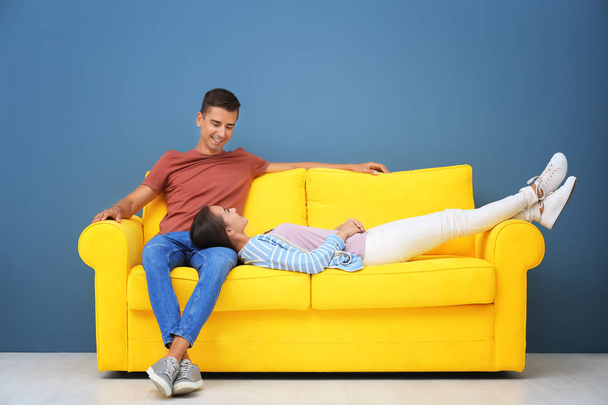 Молодая пара на желтом диване возле стены цвета
 - Фото, изображение