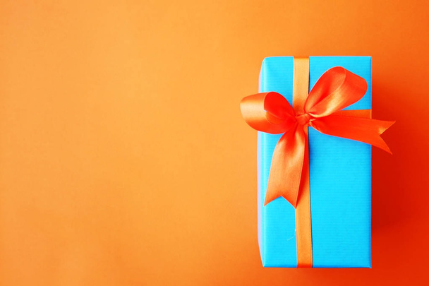 Gift or present box wrapped in blue paper and orange ribbon on color table top view. Flat lay. Copy space for text. - Valokuva, kuva