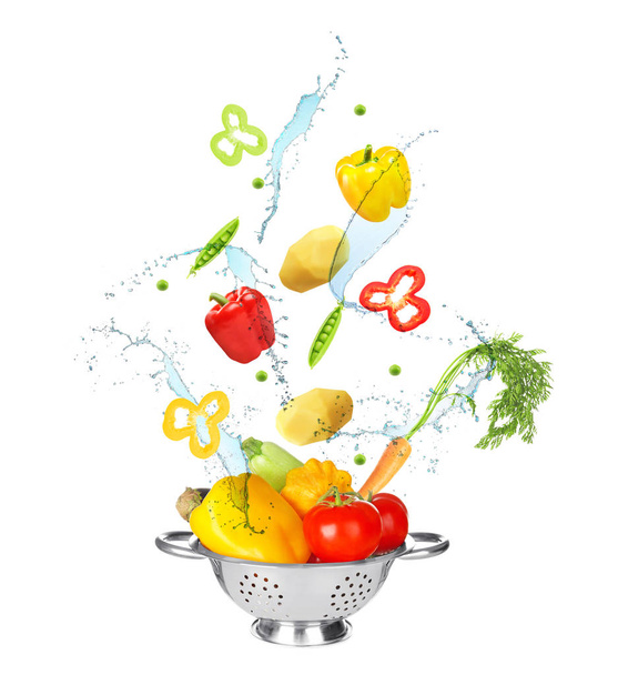 Different vegetables, water splashes and colander on white background - Фото, изображение