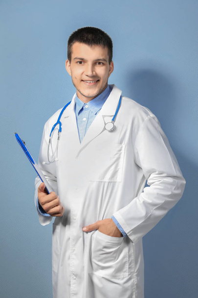 Young male doctor with clipboard against color background - Photo, Image