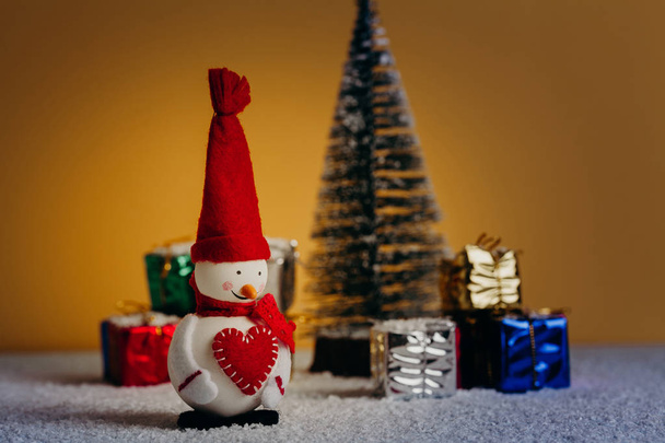 Christmas still life with snowman, tree and gifts. Snowy floor and night lights. - Photo, image