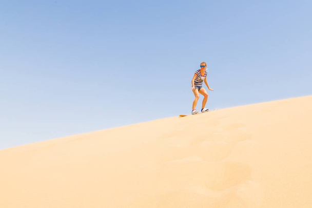Woman sandboarding down the dune in a desert - Fotoğraf, Görsel