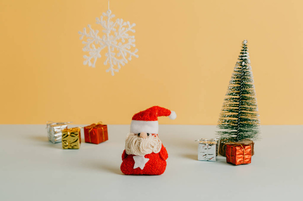 Christmas card with Santa toy, christmas tree and gifts with a snowflake and cream yellow color background. - Foto, Imagem