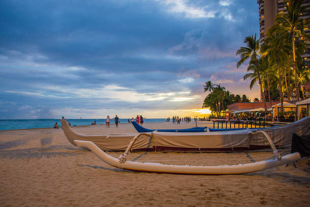 atemberaubender Blick auf den Sonnenuntergang vom Strand von Waikiki mit blauem Himmel und einem traditionellen Segelboot, das am Ufer festgemacht hat. - Foto, Bild
