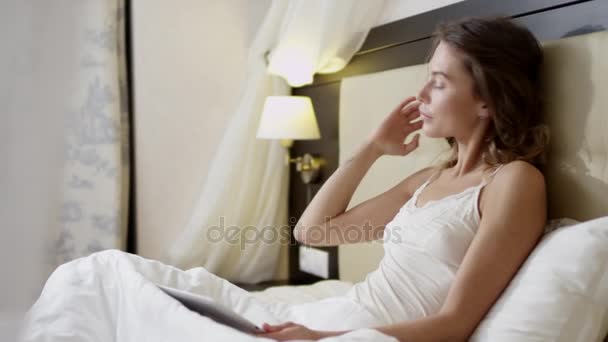 Young woman lying in bed taking a photo of herself by using tablet pc - Séquence, vidéo
