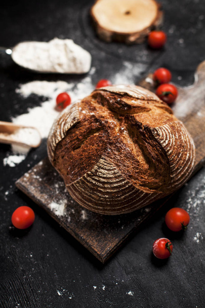 freshly baked bread, flour and tomatoes on a wooden board on a table - Photo, Image