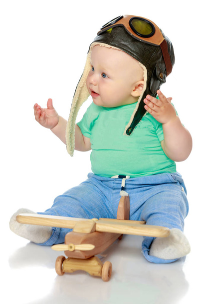 A little boy in a pilots cap and a wooden plane in his hand - Zdjęcie, obraz