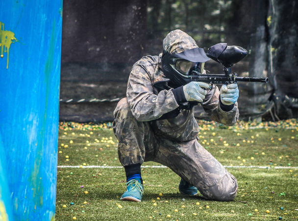 Giocatore sportivo di paintball in uniforme protettiva e maschera che gioca con la pistola all'aperto - Foto, immagini