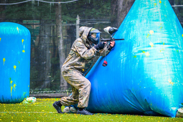 paintball sport player in protective uniform and mask playing with gun outdoors - 写真・画像