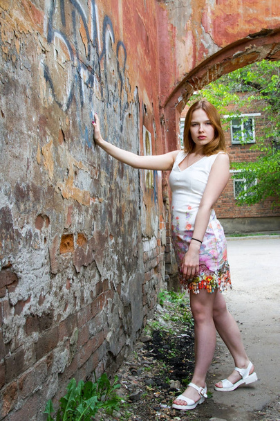Red-haired girl against the shabby wall of a dilapidated house - Photo, Image