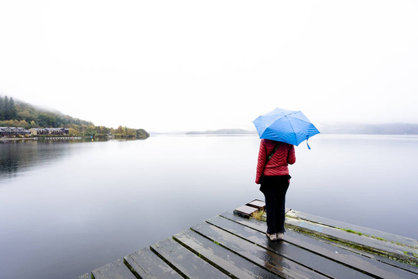 woman standing at lake keeping umbrella under the rain - Photo, Image
