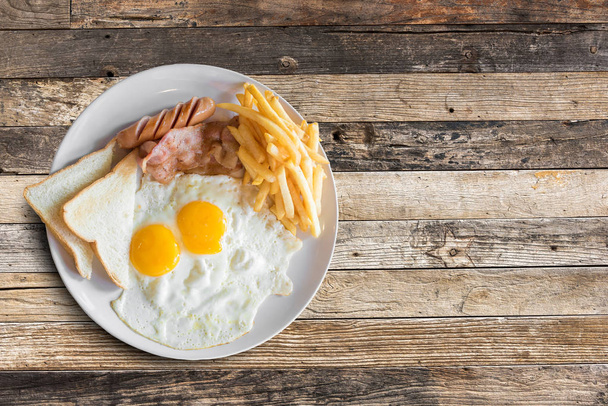 Pohled shora americká snídaně s míchanými vejci, slaninou, toast, hranolky a párek na dřevěný stůl pozadí. - Fotografie, Obrázek