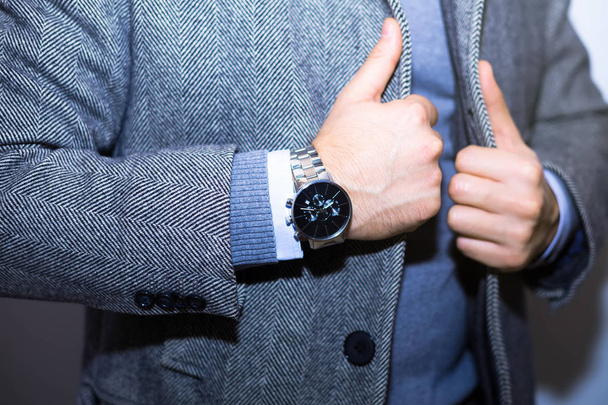 Fashion portrait of young businessman handsome model man in casual cloth suit with accessories on hands.wearing black jacket,steel watches,black vest,grey wool coat. - Foto, afbeelding