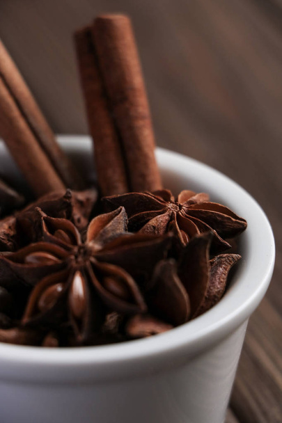 two cinnamon sticks, anise stars and coffee beans in one white ceramic bowl at brown wooden table, ingredients for delicious coffee or mulled wine - Photo, Image