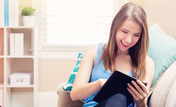 Happy young woman reading an e-book on her couch - Foto, Imagem