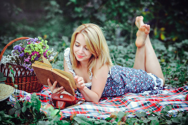 Kaunis nuori nainen piknikillä maaseudulla. Hyvää kodikasta päivää ulkona. Avaa ovi. Hymyilevä nainen kirja kädessään, rentouttava puistossa. virkistys
 - Valokuva, kuva