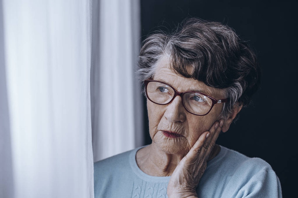 Elderly woman looking through window - Valokuva, kuva