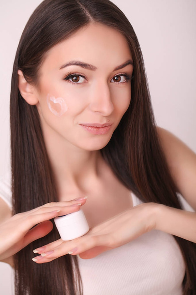 beauty, people, skincare and cosmetics concept - happy young woman with moisturizing cream on hand and facial - Photo, Image