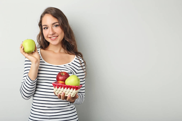Portrait of young woman with apples on grey background - Foto, Imagen