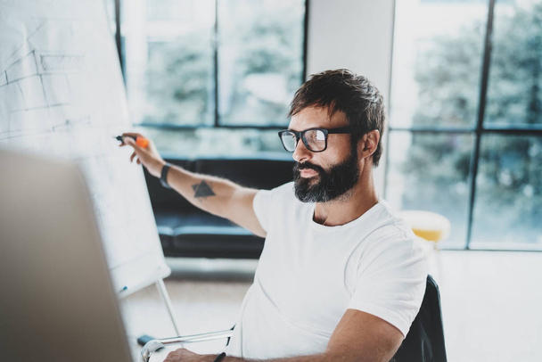 Young bearded man wearing eye glasses and working at sunny office.Blurred background. Horizontal. Cropped. - Фото, зображення