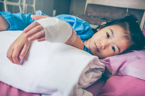 Illness asian child admitted in hospital with saline intravenous (IV) drip on hand. - 写真・画像