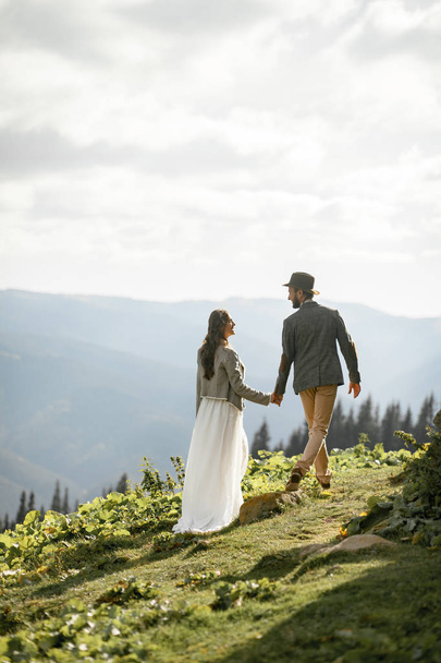 Newlyweds walk and hold hands in mountains. - Foto, Imagen