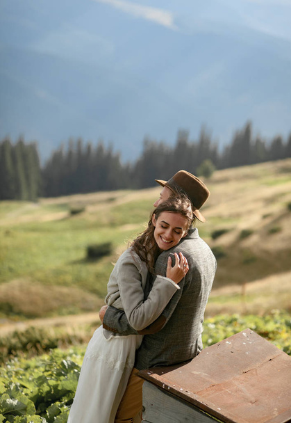 Newlyweds stand, smile and hug on background of mountains. - Фото, зображення