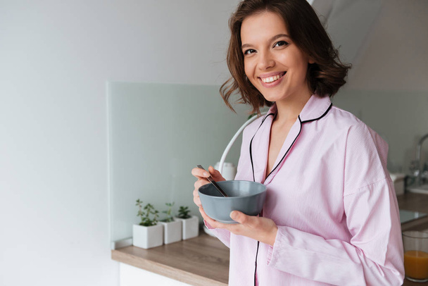 Portrait of a smiling young girl in pajamas having breakfast - Foto, imagen