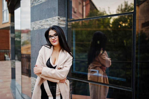 Black hair sexy woman in glasses and coat posed against building - Zdjęcie, obraz