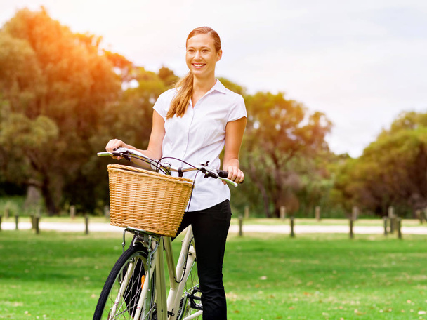 Beautiful young blond woman with bike in park - Фото, изображение