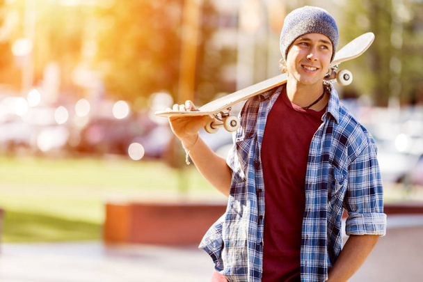 Teenage boy with skateboard standing outdoors - Foto, Bild