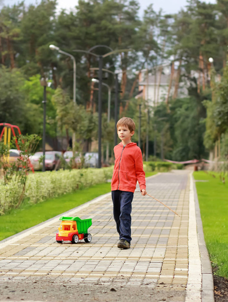 Niño de cinco años jugando y tirando de un camión de colores brillantes entre la vegetación en el parque
 - Foto, Imagen