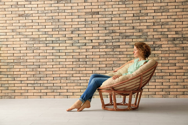 Young woman resting in lounge chair near brick wall - Фото, зображення