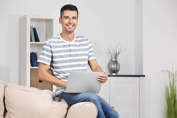 Young man with modern laptop on sofa at home - Φωτογραφία, εικόνα