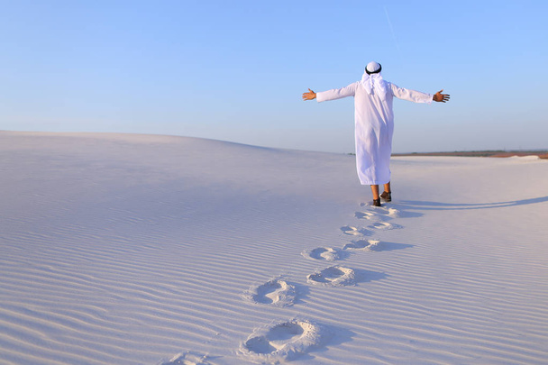 Alegre macho musulmán camina por el desierto de arena blanca y disfruta li
 - Foto, Imagen