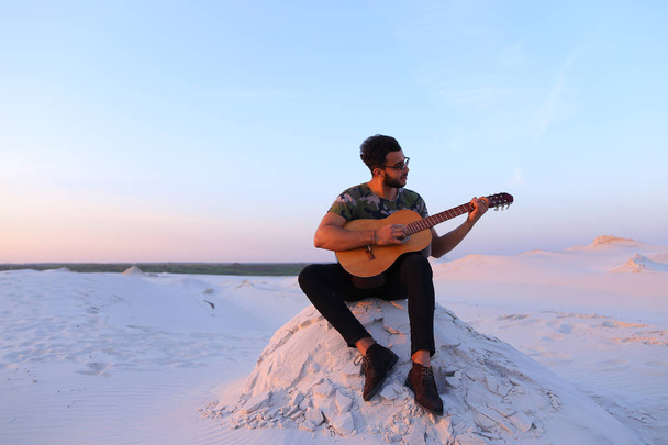 Attractive Arabian guy sings songs on guitar, sitting on hill in - Photo, Image
